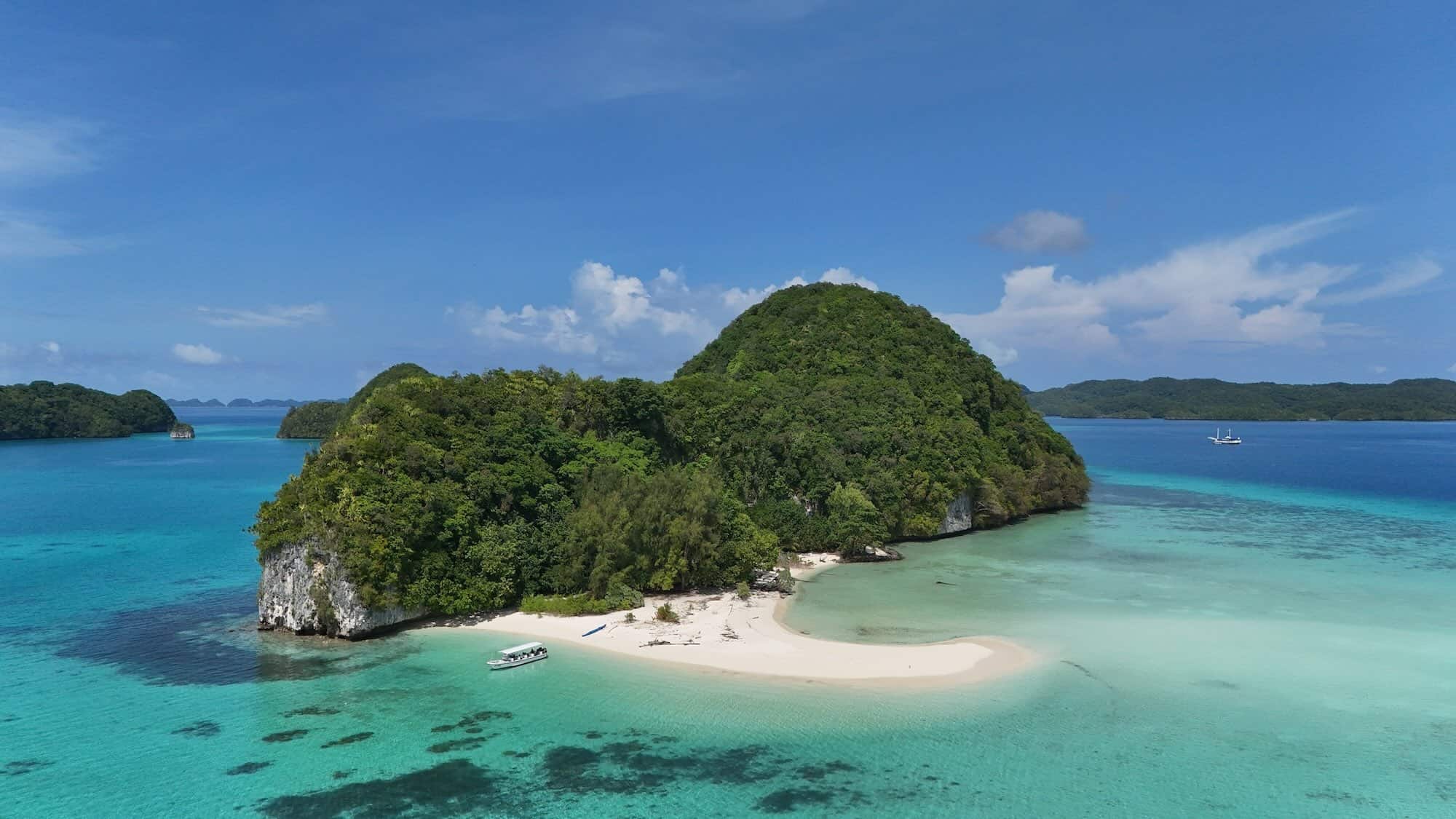 Aerial view of Palau's dramatic Rock Islands, featuring jagged limestone karsts rising from turquoise lagoons, with a small boat anchored nearby as colorful snorkelers dive into the crystal-clear waters teeming with coral reefs.